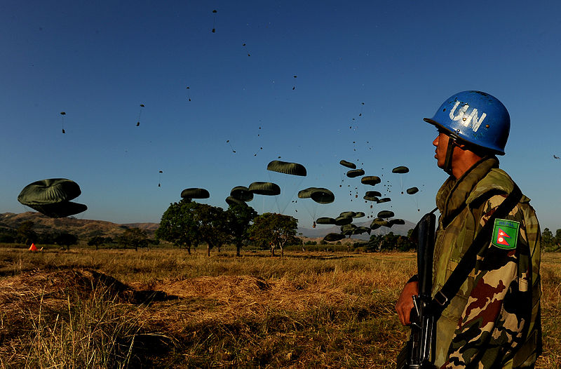 A Nepalese soldier patrolling while pallets of humanitarian aid drop in Haiti.