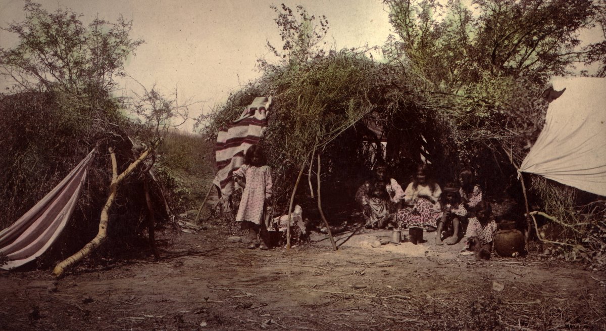 A Chiricahua Apache medicine man with his family inside a brush wickiup.