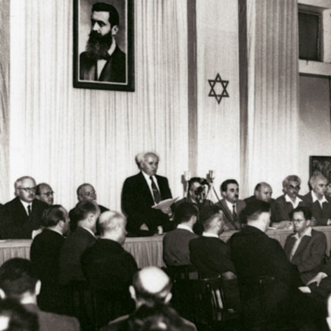David Ben-Gurion proclaiming Israel's independence beneath a large portrait of Theodor Herzl.