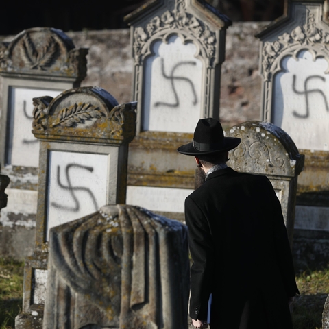 A Jewish man looking at gravestones that have been spray painted with swastikas