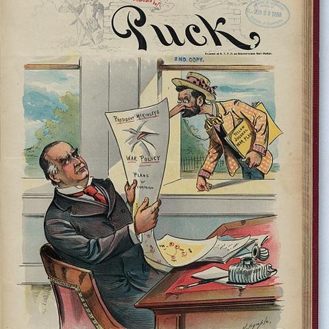The cover from Puck depicts President William McKinley at his desk examining his war policy.