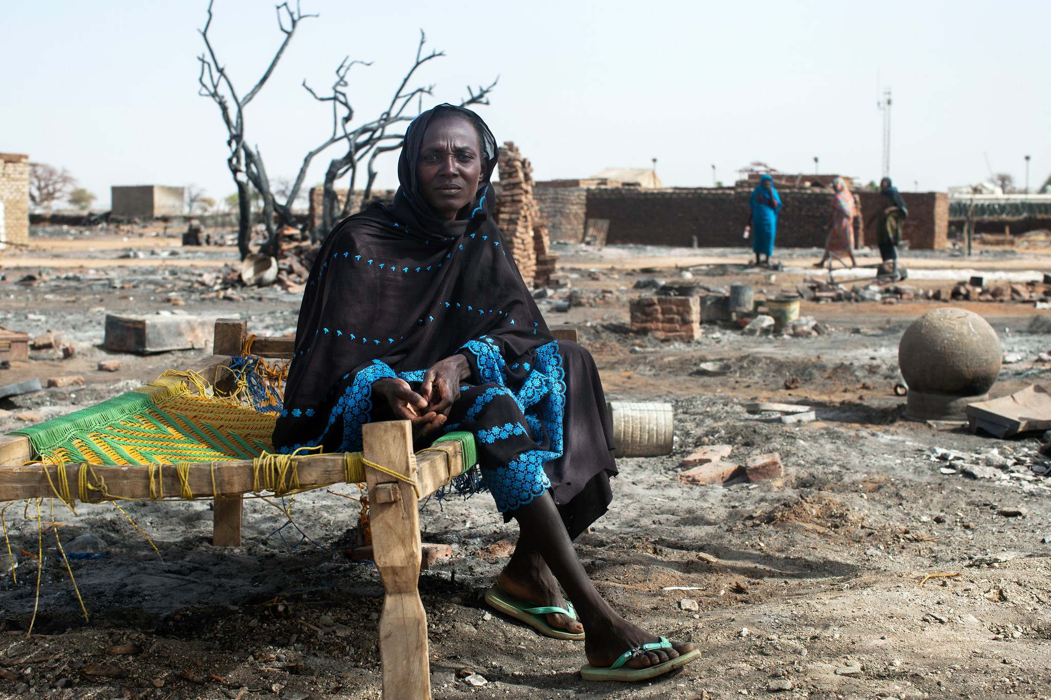 A displaced woman sits on a bed next to the remnants of her burnt house in Khor Abeche, South Darfur, 2014. UN Photo/Albert Gonzalez Farran, UNAMID