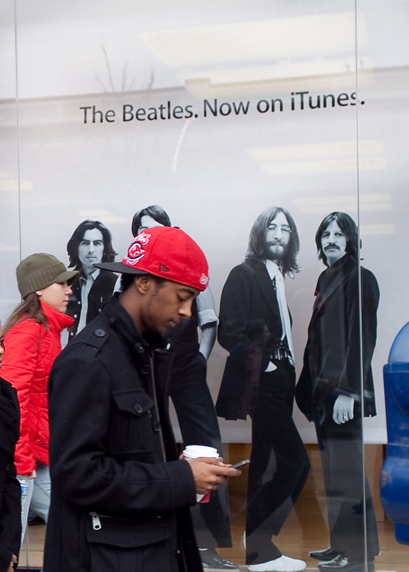 A young man stays connected on his cell phone as he strolls by a store advertising the Beatles' music on Apple's online store.