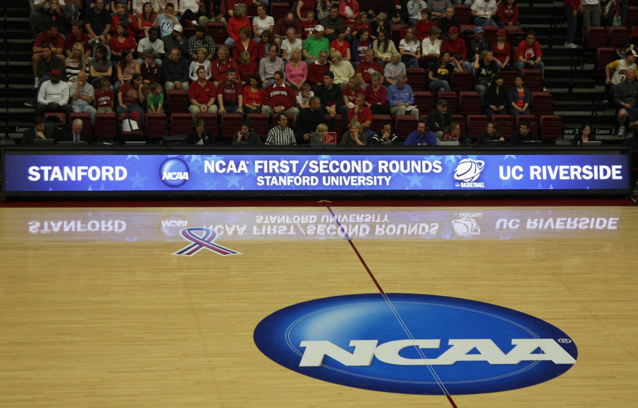 The National Collegiate Athletic Association (NCAA)'s logo at the center of a collegiate basketball court.