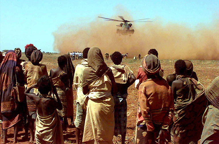 Somalis from the village of Maleel watch a US Marine Helicopter deliver wheat donated by the people of Australia, 1992. 