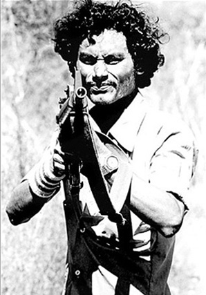 A Farabundo Martí National Liberation Front (FMLN) soldier takes aim during a wartime “road advisory” near Suchitoto, El Salvador (1984). Photo by Gary Mark Smith.
