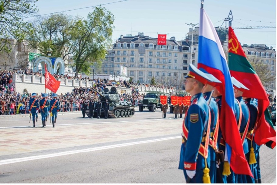The Pridnestrovian and Russian flags stand together as symbols of Soviet military glory pass by. Tiraspol, May 9th, 2021.