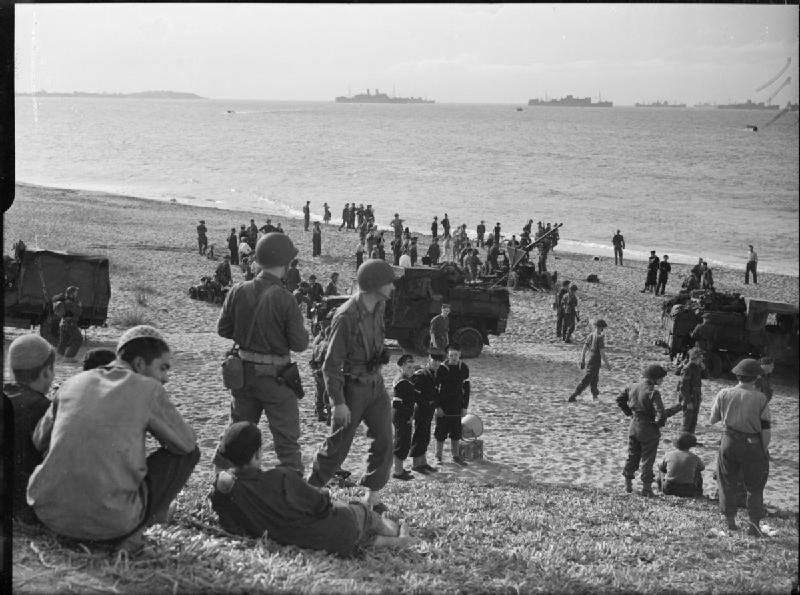 British soldiers and sailors stand with American soldiers on the beach near Algiers.