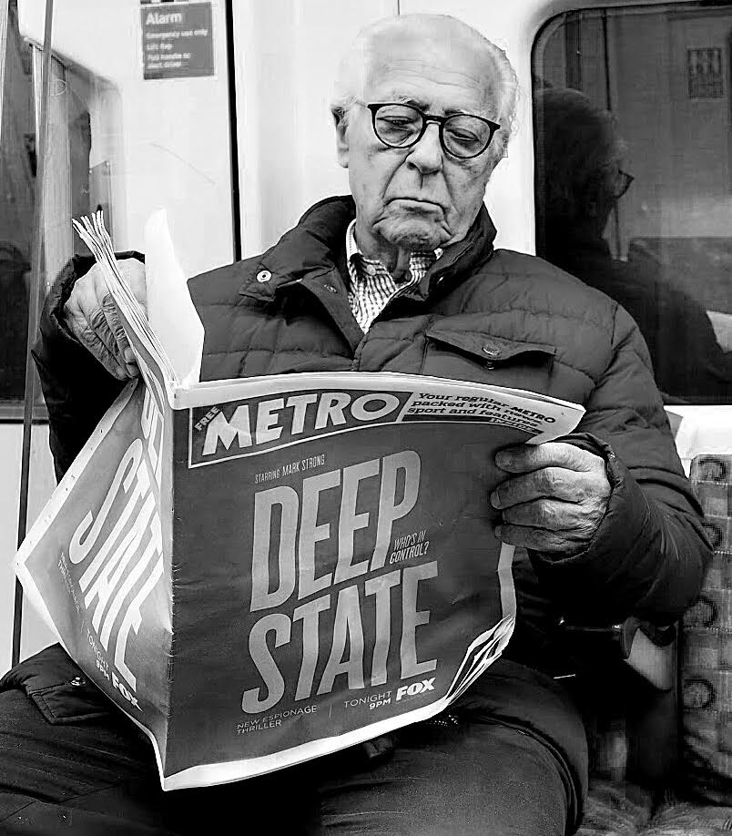 Man reading a newspaper with the headline "Deep State", 2018.