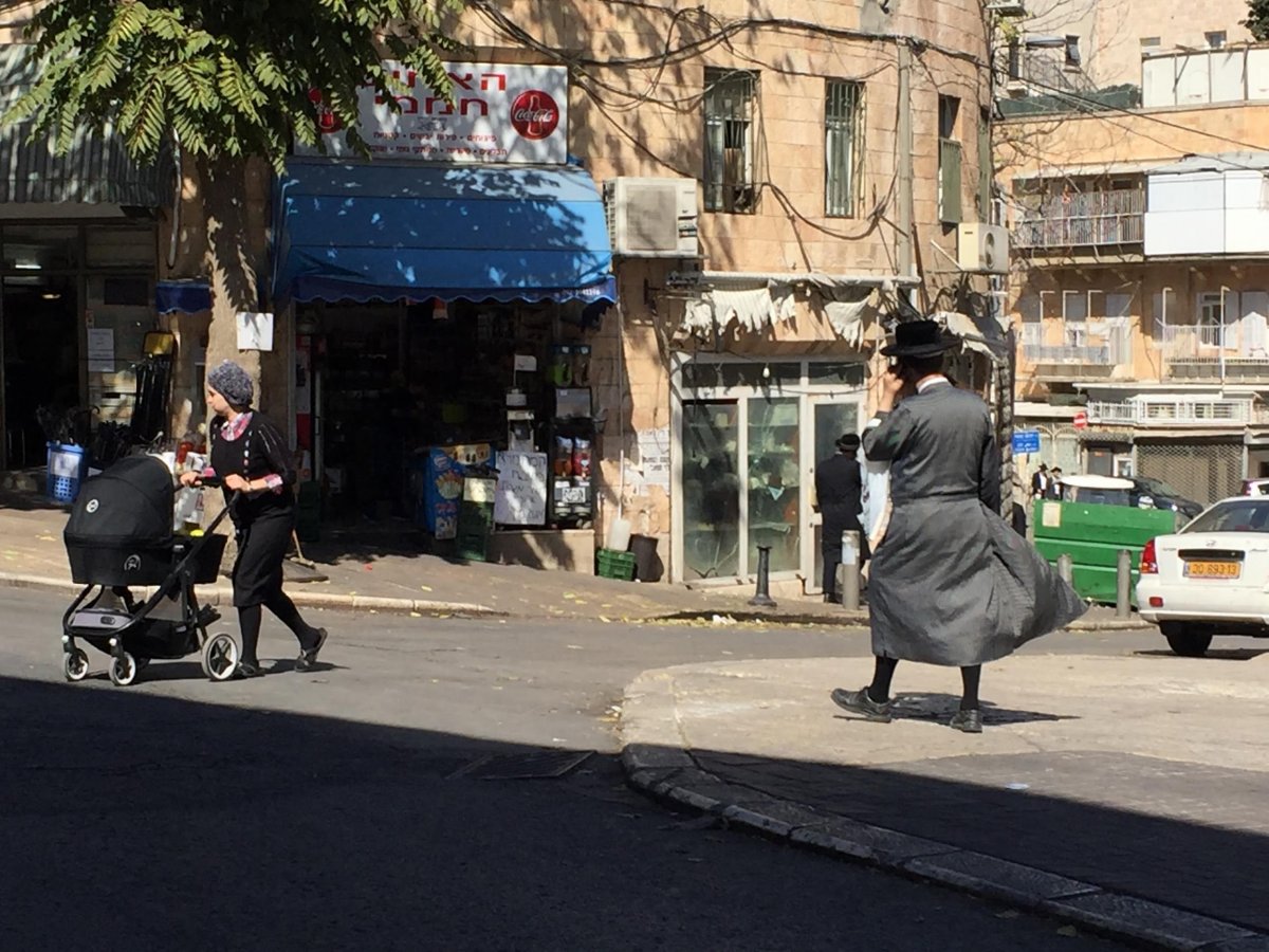 An ultra-Orthodox mother pushes her child while an ultra-Orthodox man walks by.