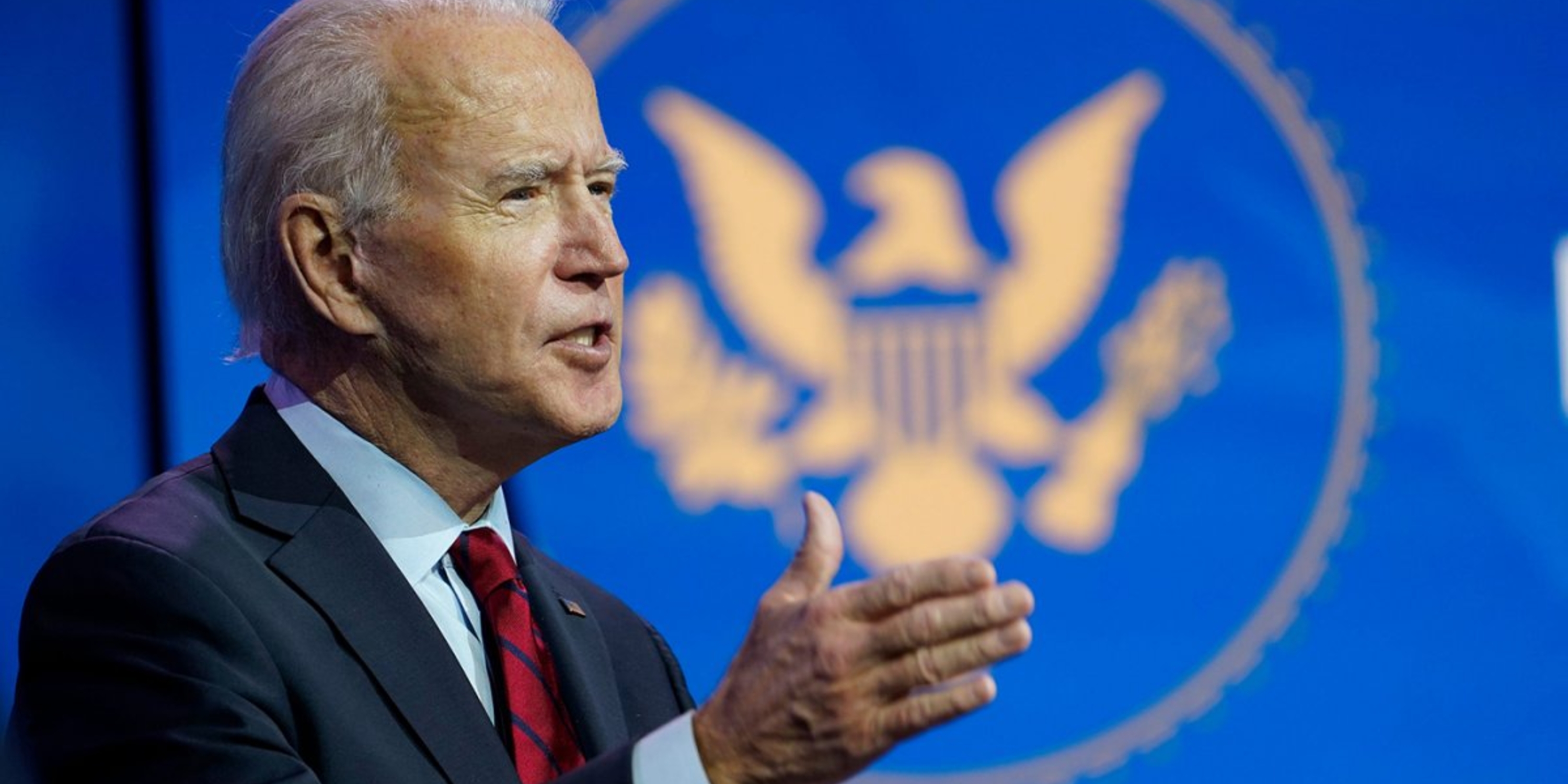 President Biden, standing in front of a blue flag with an eagle emblem