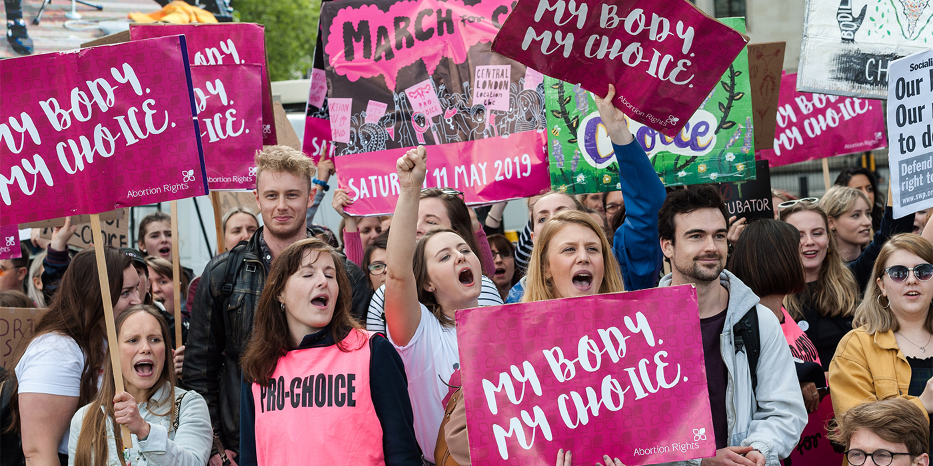 A group of men and women. The women hold signs that say "My Body, My Choice"