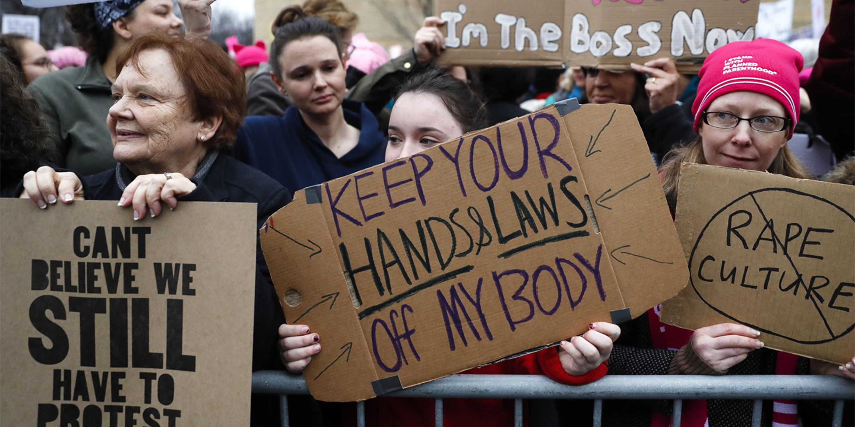 Women at the Women's March in DC with signs: "Can't Believe We STILL Have to Protest", "Keep your Hands and Laws Off my Body", "RAPE CULTURE" with a line through it