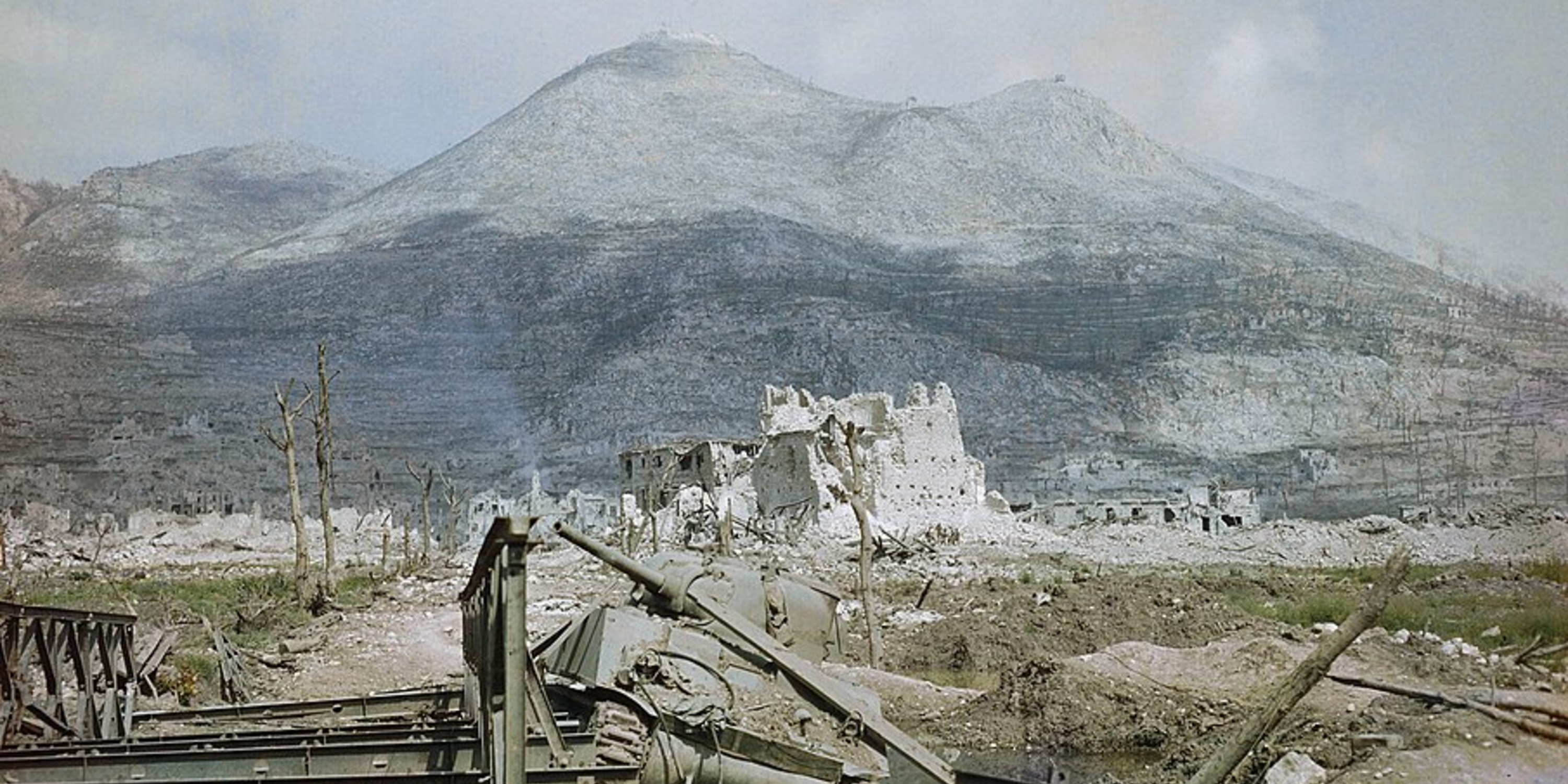 The ruins of Cassino, May 1944 - a wrecked Sherman tank and Bailey bridge in the foreground, with Monastery Ridge and Castle Hill