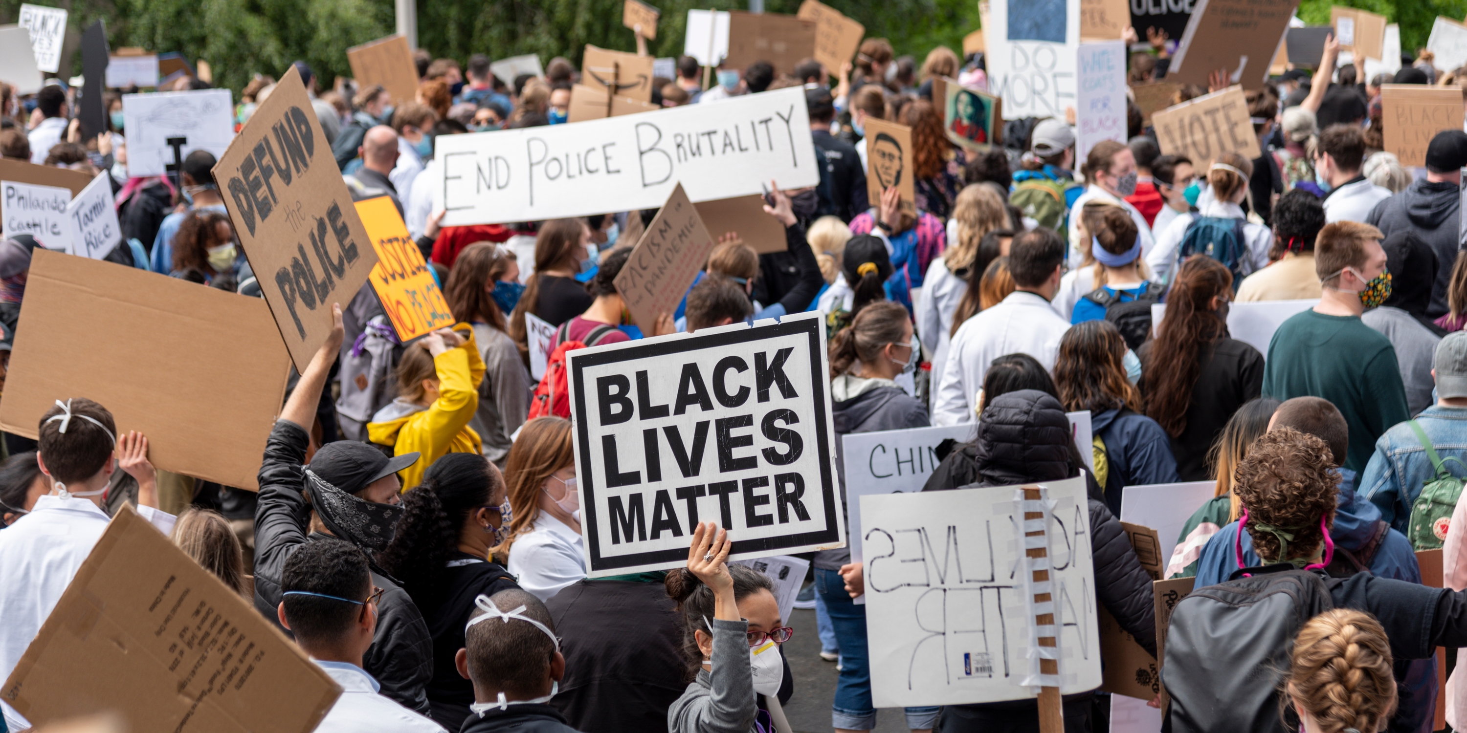 a crowd of people holding signs. some signs read "Black Lives Matter" and "End Police Brutality" and Defund the Police"