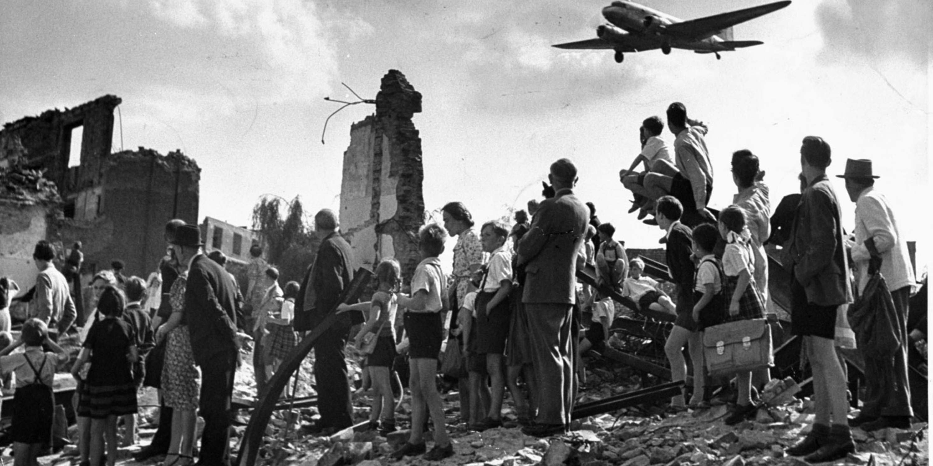 West Berliners stand amid the rubble of WWII and watch U.S. Air Force transport planes land at Templehof Airport during the Berlin Airlift in 1948. 