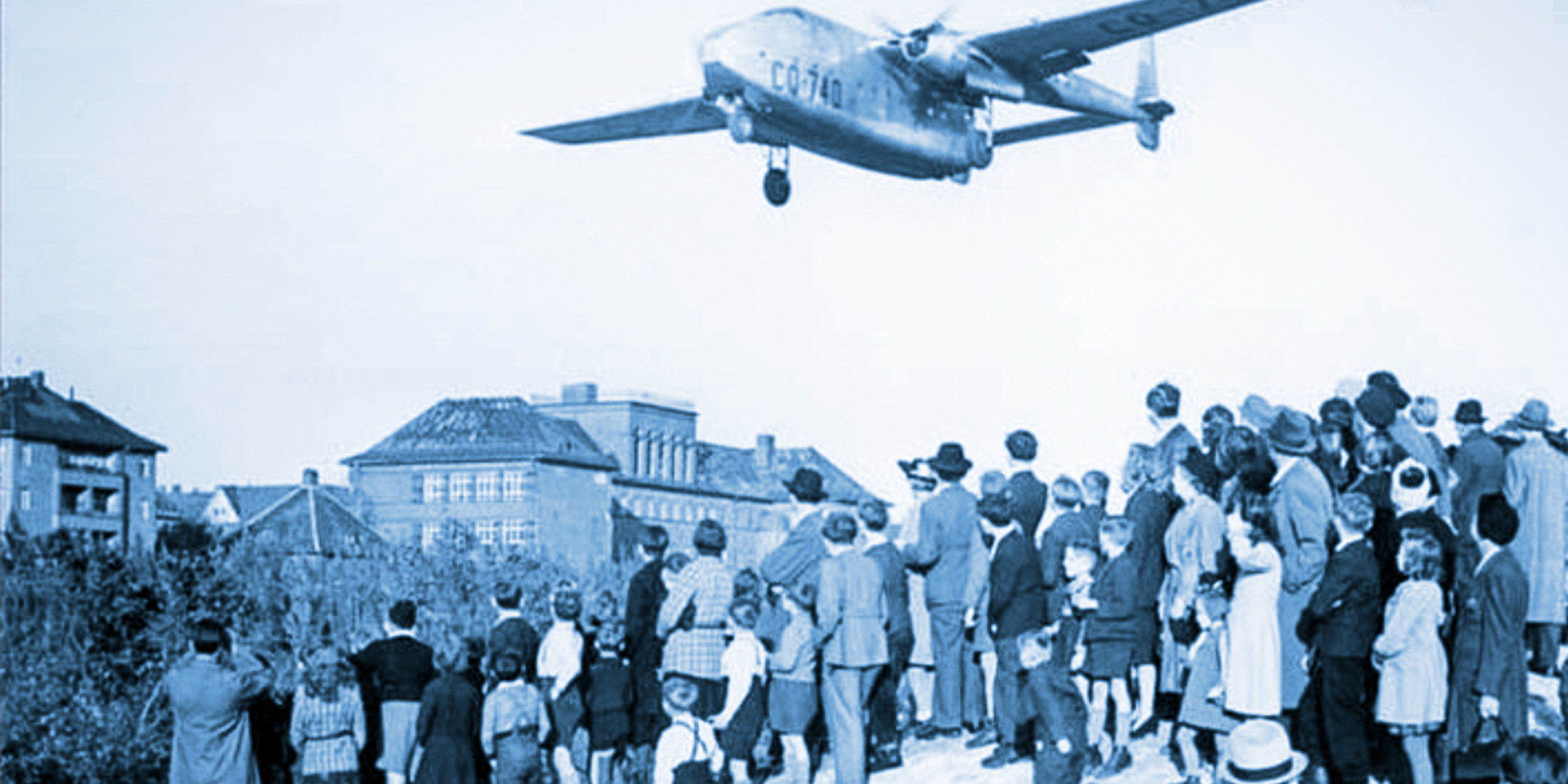 a plane flying over a group of West Berlin citizens