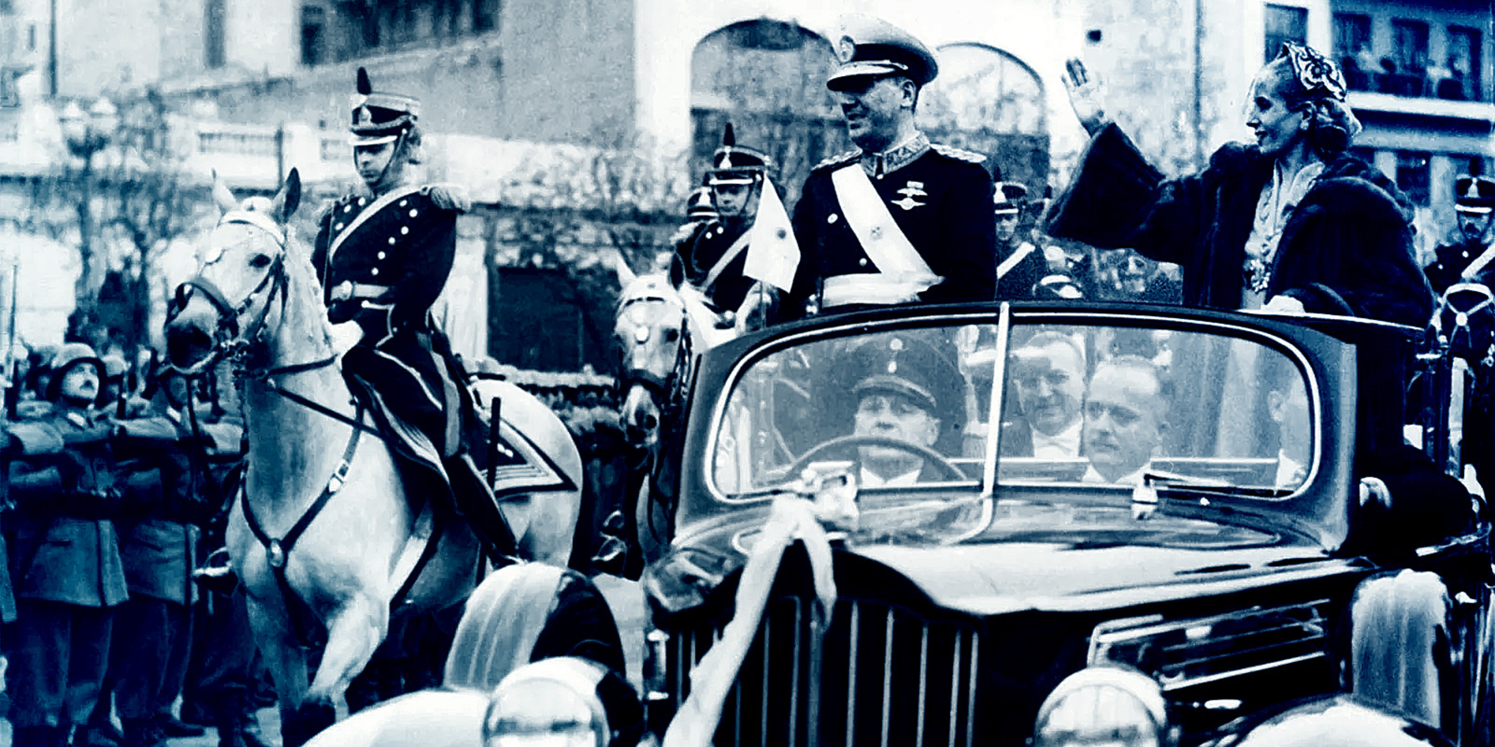 Juan and Evita Perón standing in a car waving, a soldier on horseback is beside the car