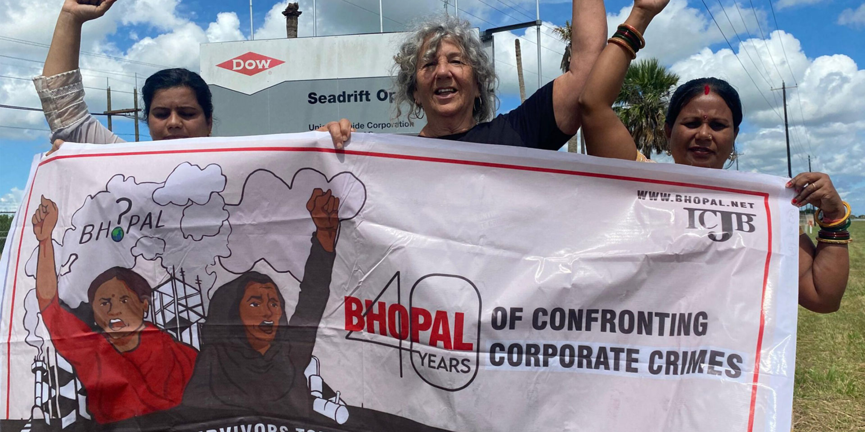 women with hands raised in air holding a sign protesting the Bhopal Chemical disaster