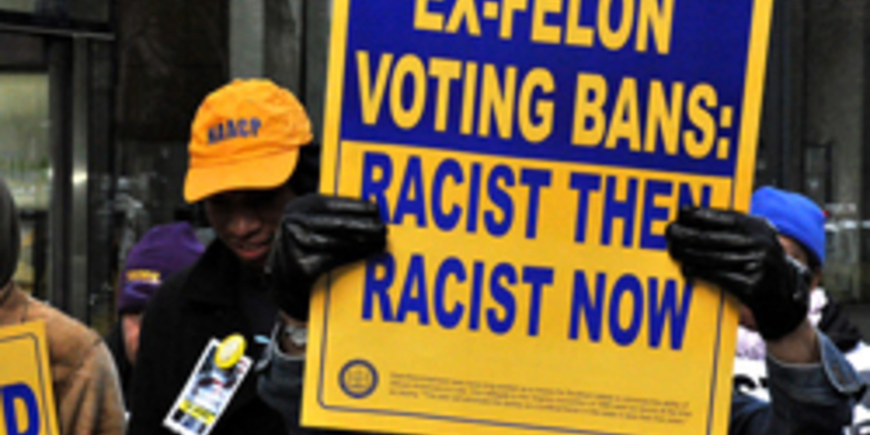 person holding sign that says ex-felon voting bans - racist then racist now