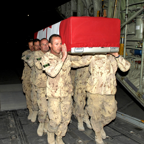 Canadian Troops load a coffin into a transport plane.