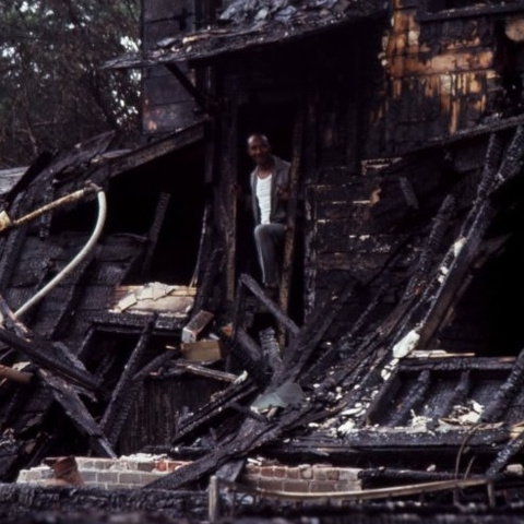 African American man stands in doorway of burned-out building, 1967.  
