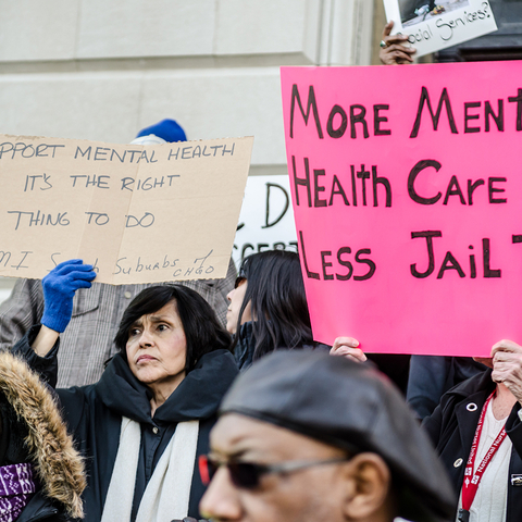 People holding signs: "More Mental Health Care + Less Jail Time" and "Support Mental Health - It's the Right Thing to Do"