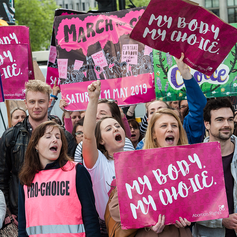 A group of men and women. The women hold signs that say "My Body, My Choice"