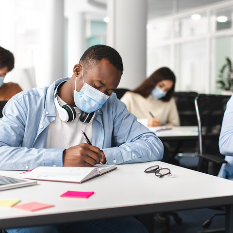 students wearing masks sitting at desks in a classroom writing