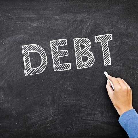 the word Debt written on a blackboard with chalk and a hand holding chalk that is pointing to it