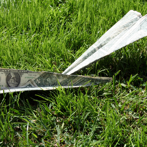 two paper airplanes made out of dollar bills, laying on green grass