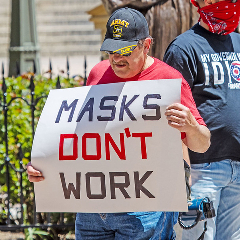 a man holding a sign that reads - Masks Don't Work