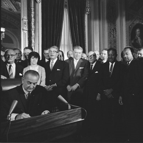 President Lyndon B. Johnson signing the Voting Rights Act as MLK and other civil rights leaders look on.