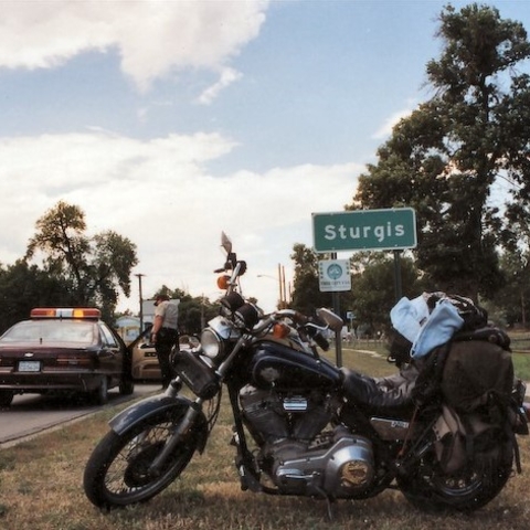 A motorcycle parked in front of the Sturgis city limit sign.
