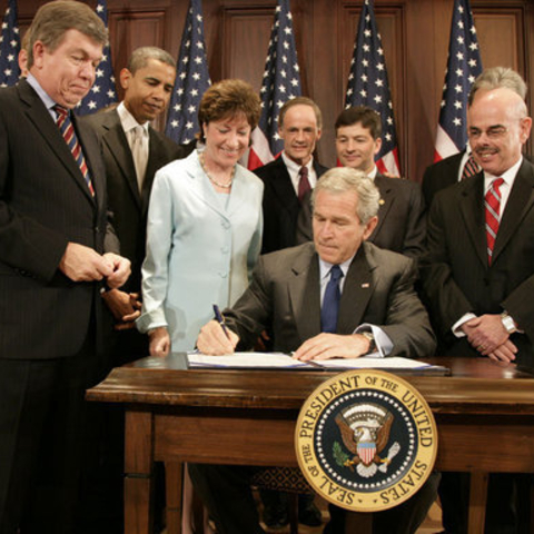 President George W. Bush signs a law in front of senators. 