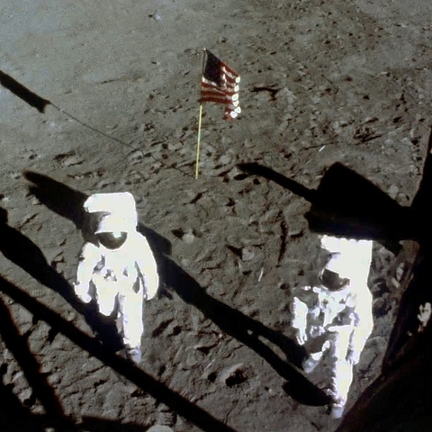 Neil Armstrong and Buzz Aldrin walking on the moon in 1969 with the American flag behind them.