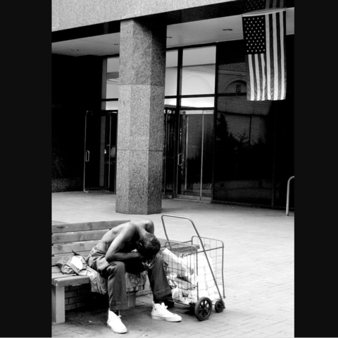 A homeless man outside the outside the United Nations building in New York with the American flag in the background.