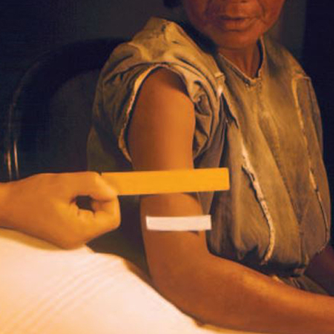 Someone's hand holding a paper strip up to a Guatemalan woman's arm. The woman's arm has a white strip on it.