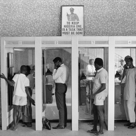 Nigerians use phone booth under a poster against Biafran separatists and their leader, General C. Odumegwu Ojuku. 1967.