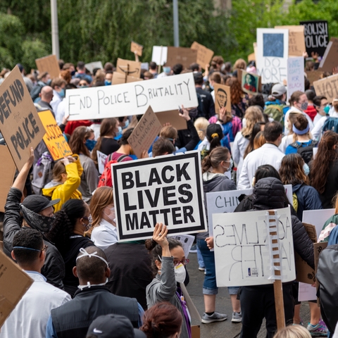 a crowd of people holding signs. some signs read "Black Lives Matter" and "End Police Brutality" and Defund the Police"