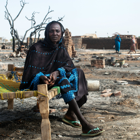 A displaced woman sits on a bed next to the remnants of her burnt house in Khor Abeche, South Darfur, 2014. UN Photo/Albert Gonzalez Farran, UNAMID