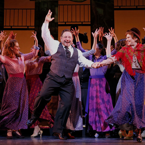 People dancing in a Broadway musical with their hands in the air