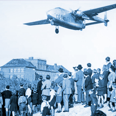 a plane flying over a group of West Berlin citizens