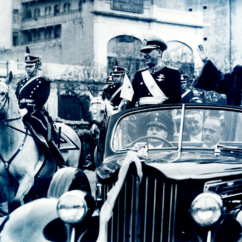 Juan and Evita Perón standing in a car waving, a soldier on horseback is beside the car