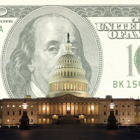 The U.S. Capitol building lit up at night in front of a one hundred U.S. dollar bill. 