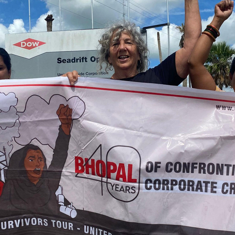 women with hands raised in air holding a sign protesting the Bhopal Chemical disaster