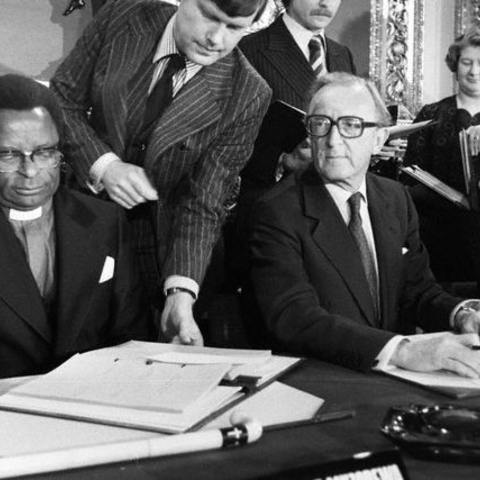 Bishop Abel Muzorewa signs the Lancaster House Agreement seated next to British Foreign Minister Lord Peter Carrington, 1979