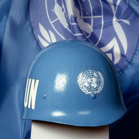 The iconic blue helmet worn by United Nations peacekeeping personnel in front of a U.N. flag.