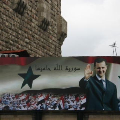 Billboard with portrait of Bashshar al-Asad and the text "God protects Syria" on the old city wall of Damascus in 2006 Source: photo by Bertil Videt
