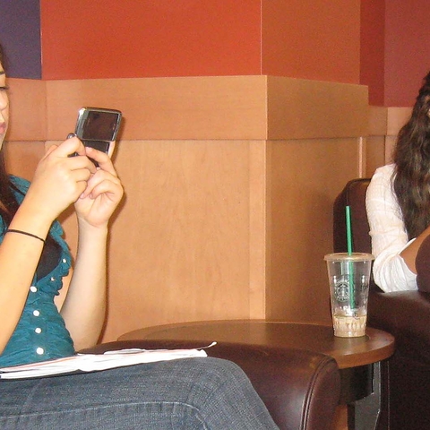 Two women sending text messages on their cell phones in a coffee shop at the California State University, Fullerton.